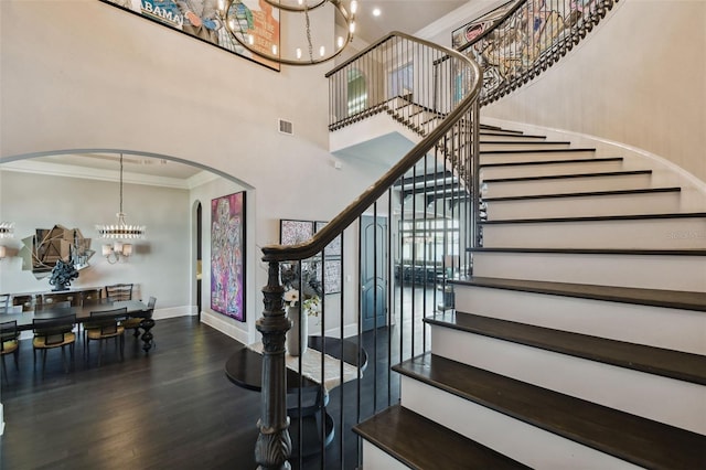 stairs featuring a towering ceiling, hardwood / wood-style flooring, crown molding, and a notable chandelier