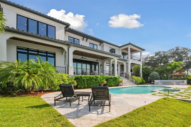 rear view of property featuring ceiling fan, a pool with hot tub, a balcony, a yard, and a patio area