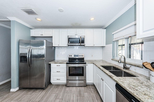 kitchen with white cabinets, appliances with stainless steel finishes, light stone countertops, and sink