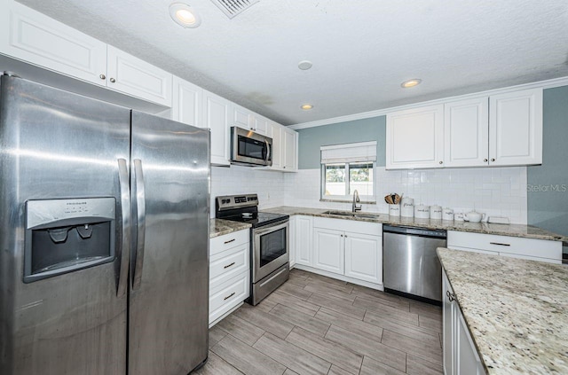 kitchen with sink, ornamental molding, light stone counters, white cabinetry, and stainless steel appliances