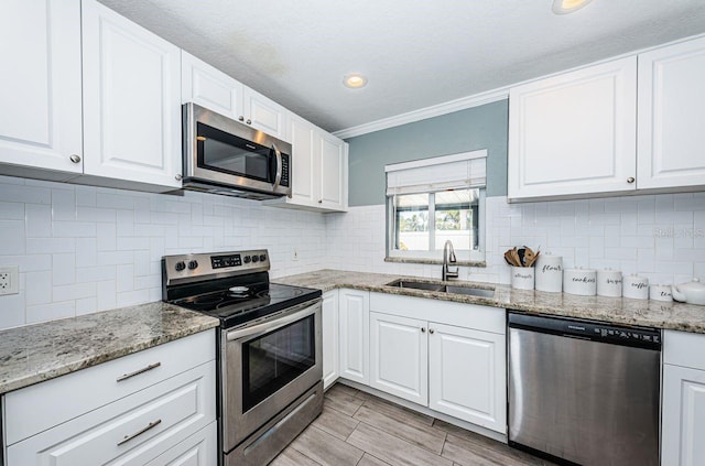 kitchen with appliances with stainless steel finishes, light stone counters, ornamental molding, sink, and white cabinetry