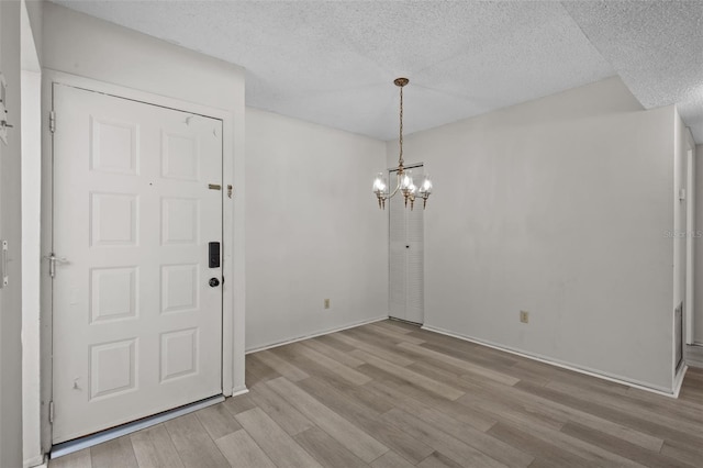 unfurnished dining area featuring a chandelier, a textured ceiling, and light hardwood / wood-style flooring