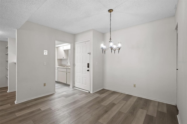 unfurnished dining area with a textured ceiling, a notable chandelier, and hardwood / wood-style flooring