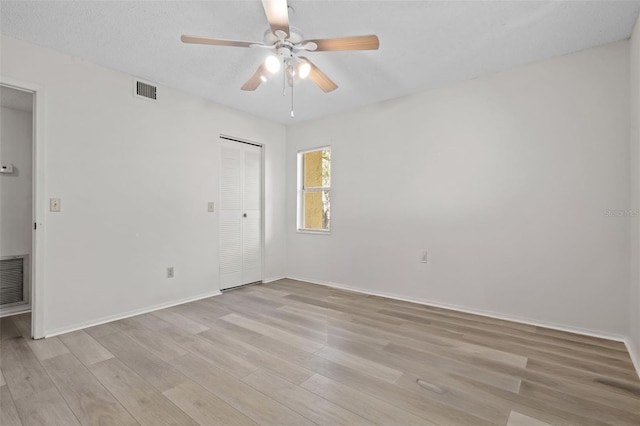 empty room featuring ceiling fan, light wood-type flooring, and a textured ceiling