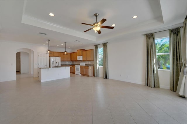 kitchen with a tray ceiling, tasteful backsplash, an island with sink, and white appliances