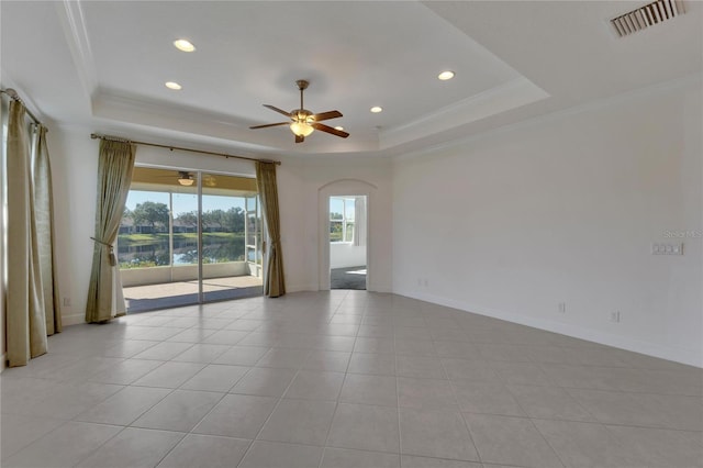 tiled empty room featuring ceiling fan, a raised ceiling, crown molding, and a water view