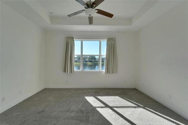 carpeted spare room featuring a raised ceiling, ceiling fan, and a water view