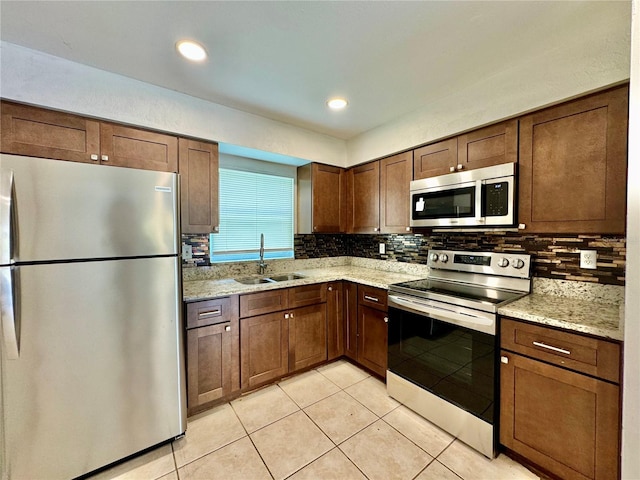 kitchen with sink, light stone countertops, appliances with stainless steel finishes, tasteful backsplash, and light tile patterned flooring