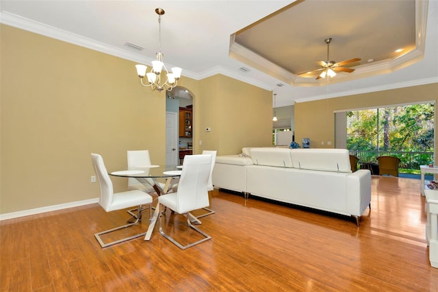 dining room with a tray ceiling, light hardwood / wood-style flooring, ornamental molding, and ceiling fan with notable chandelier