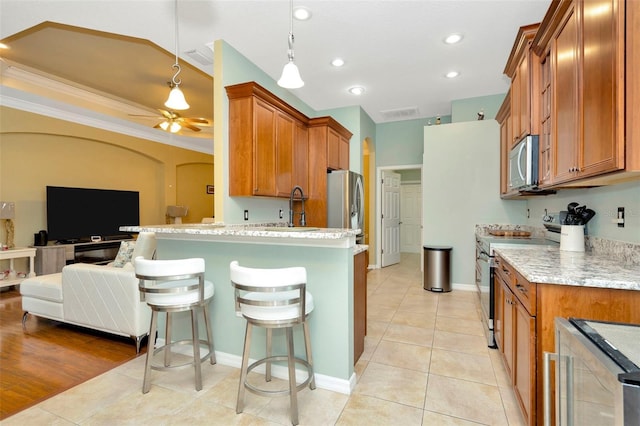 kitchen with sink, hanging light fixtures, appliances with stainless steel finishes, a kitchen breakfast bar, and light stone countertops