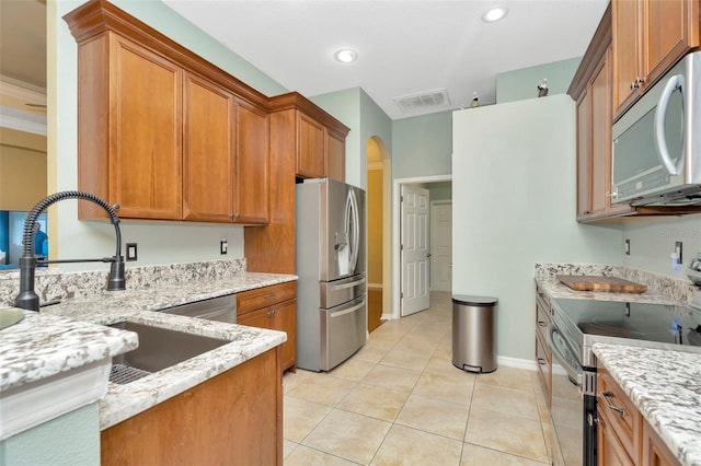 kitchen with appliances with stainless steel finishes, sink, light tile patterned floors, and light stone counters