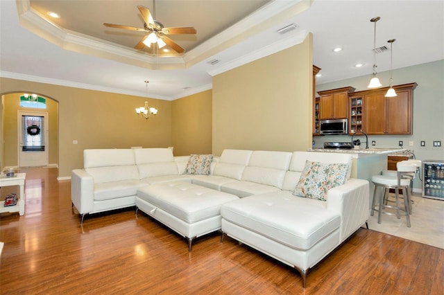 living room with dark wood-type flooring, ceiling fan, a tray ceiling, and crown molding