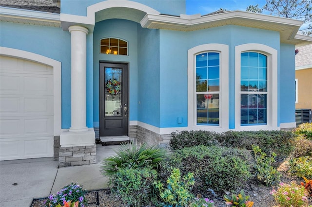 doorway to property with a garage, stucco siding, and central AC