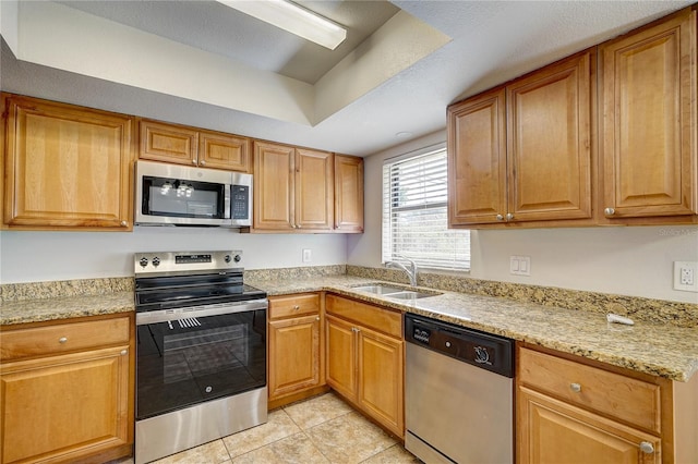 kitchen with sink, stainless steel appliances, light stone counters, a textured ceiling, and light tile patterned floors