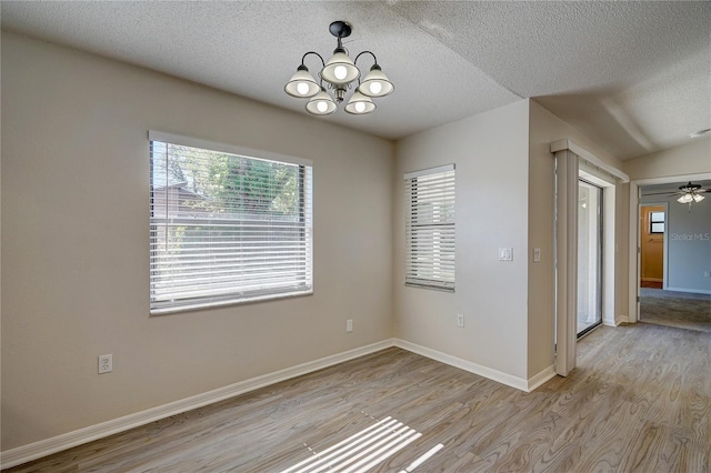 unfurnished room featuring lofted ceiling, ceiling fan with notable chandelier, light hardwood / wood-style floors, and a textured ceiling