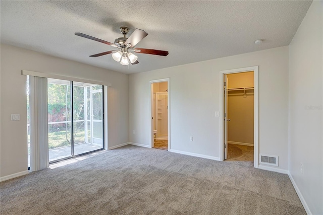 unfurnished bedroom featuring a walk in closet, a textured ceiling, light colored carpet, ceiling fan, and a closet