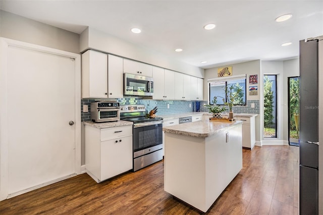 kitchen with dark hardwood / wood-style flooring, tasteful backsplash, stainless steel appliances, white cabinetry, and a kitchen island