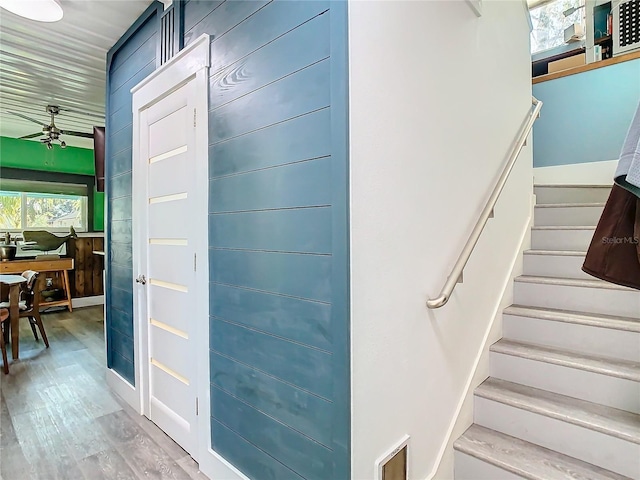 stairs with ceiling fan, hardwood / wood-style floors, and wooden walls