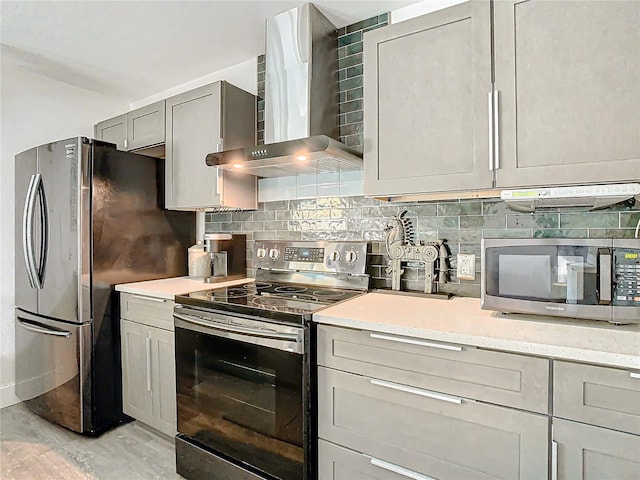 kitchen with backsplash, light stone counters, stainless steel appliances, wall chimney range hood, and gray cabinets