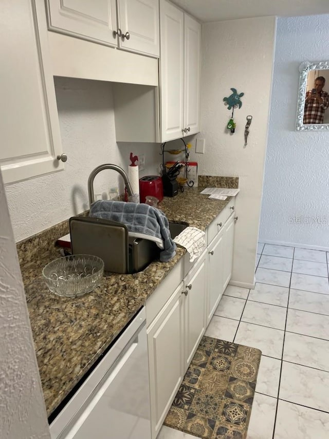 kitchen featuring white cabinets, light tile patterned flooring, stainless steel dishwasher, and dark stone countertops