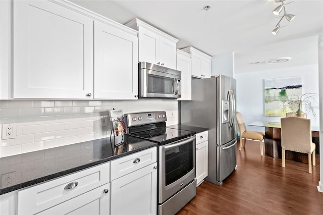 kitchen featuring decorative backsplash, stainless steel appliances, dark stone countertops, dark hardwood / wood-style floors, and white cabinetry