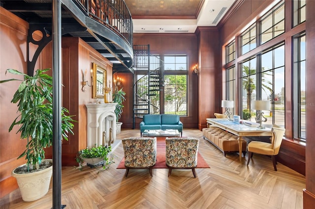 living area with wood walls, crown molding, light parquet floors, and a high ceiling