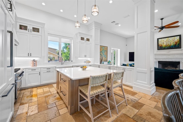 kitchen featuring ceiling fan, a center island, hanging light fixtures, stainless steel stove, and white cabinets