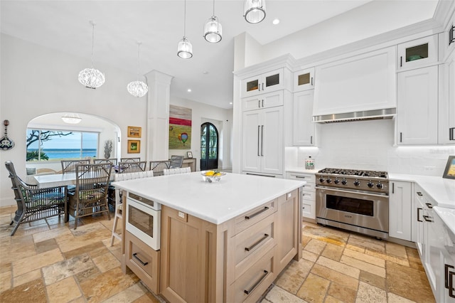 kitchen featuring light brown cabinets, white cabinetry, hanging light fixtures, and high end stainless steel range