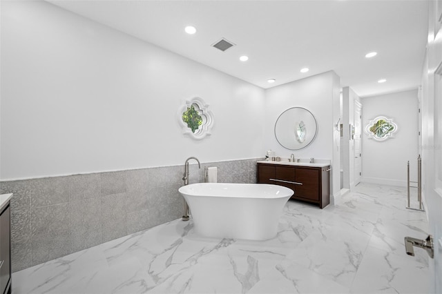 bathroom with a washtub, vanity, and tile walls