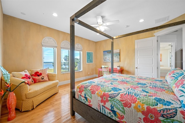 bedroom featuring light hardwood / wood-style floors, ceiling fan, and a water view