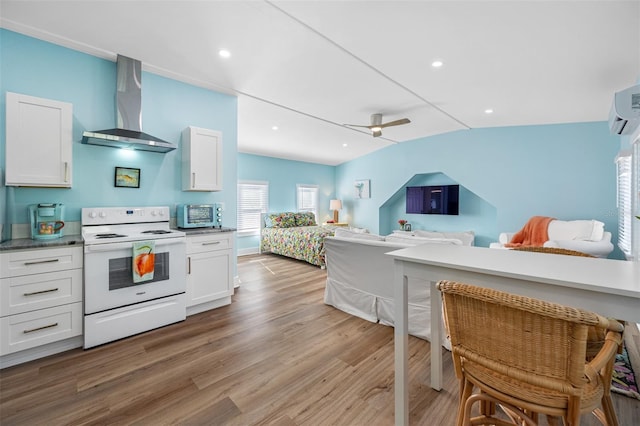 kitchen with wall chimney exhaust hood, white range with electric stovetop, light hardwood / wood-style floors, and white cabinetry