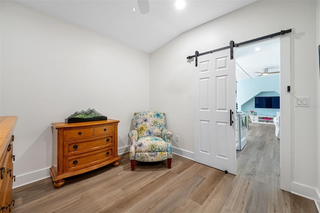 living area with vaulted ceiling, ceiling fan, a barn door, and light hardwood / wood-style floors