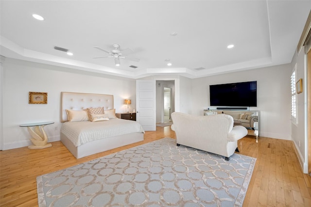 bedroom featuring a tray ceiling, light hardwood / wood-style floors, and ceiling fan