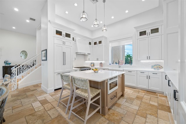 kitchen featuring custom exhaust hood, white cabinetry, built in appliances, a center island, and pendant lighting