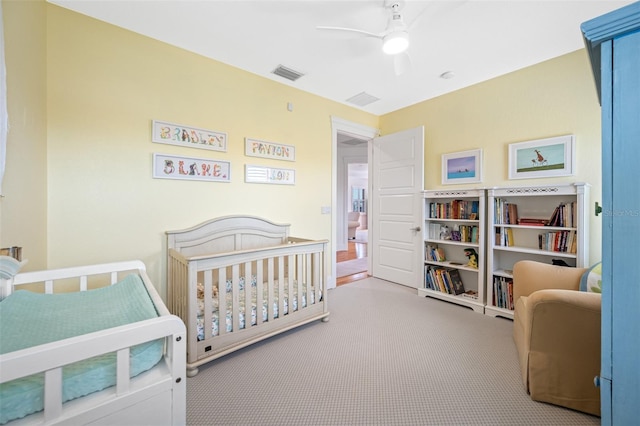 bedroom featuring a nursery area, light colored carpet, and ceiling fan