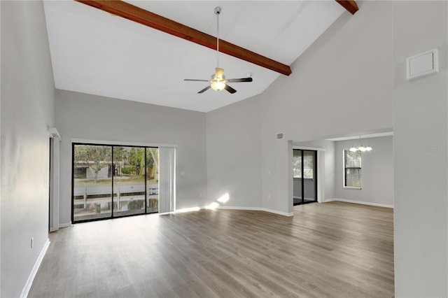 unfurnished living room featuring a healthy amount of sunlight, ceiling fan with notable chandelier, beam ceiling, and light hardwood / wood-style flooring