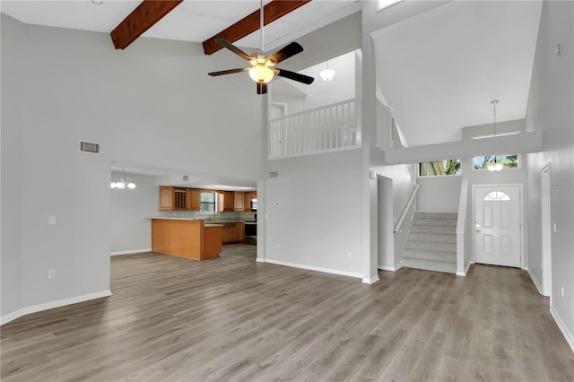 unfurnished living room featuring beam ceiling, ceiling fan with notable chandelier, a towering ceiling, and light wood-type flooring