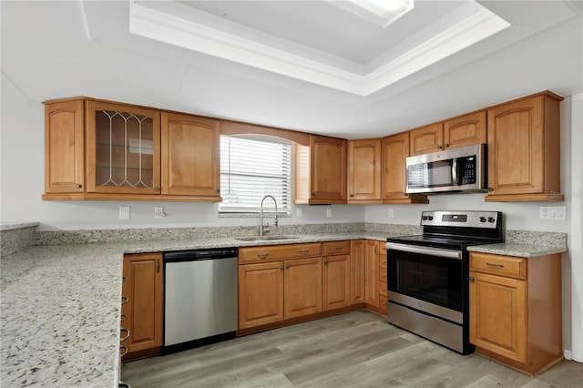 kitchen with sink, appliances with stainless steel finishes, a tray ceiling, light stone countertops, and light hardwood / wood-style floors