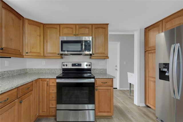 kitchen with appliances with stainless steel finishes, light stone countertops, and light hardwood / wood-style flooring