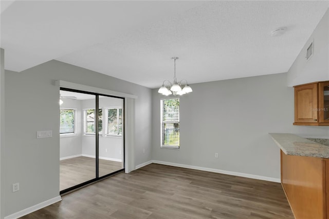 unfurnished dining area featuring a chandelier, a textured ceiling, and light wood-type flooring