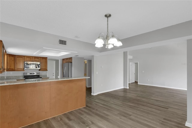 kitchen featuring stainless steel appliances, dark hardwood / wood-style floors, a tray ceiling, decorative light fixtures, and kitchen peninsula