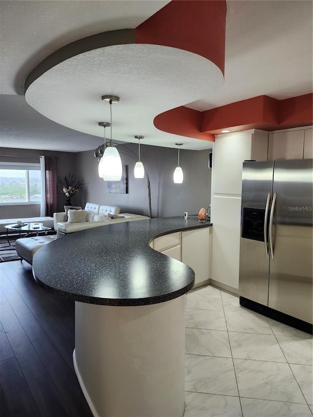 kitchen with stainless steel fridge with ice dispenser, light hardwood / wood-style flooring, hanging light fixtures, and a textured ceiling