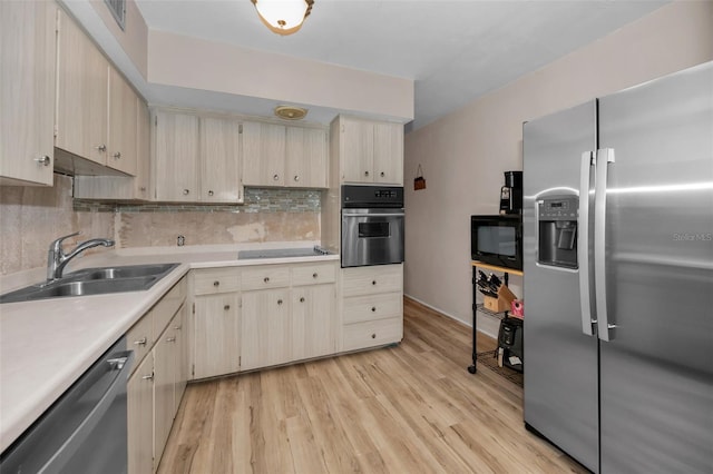 kitchen with black appliances, light wood-style flooring, a sink, tasteful backsplash, and light countertops