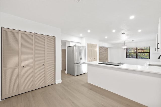 kitchen with sink, hanging light fixtures, stainless steel fridge, light hardwood / wood-style floors, and white cabinets