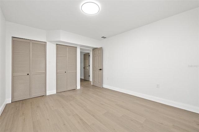 unfurnished bedroom featuring two closets and light hardwood / wood-style flooring