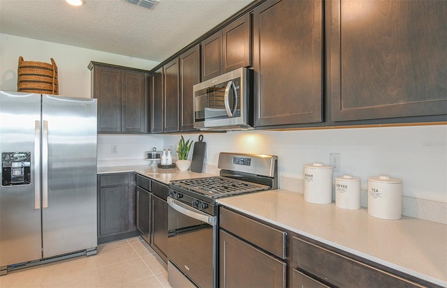 kitchen featuring appliances with stainless steel finishes, dark brown cabinetry, a textured ceiling, and light tile patterned flooring