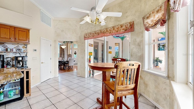 dining space featuring ceiling fan, light tile patterned floors, crown molding, and a high ceiling