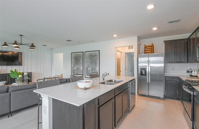 kitchen with a breakfast bar, stainless steel appliances, sink, light tile patterned floors, and a center island with sink