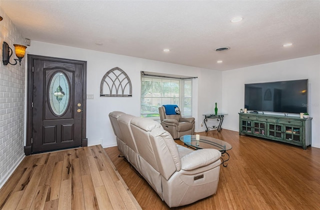 living room featuring wood-type flooring, a textured ceiling, and brick wall