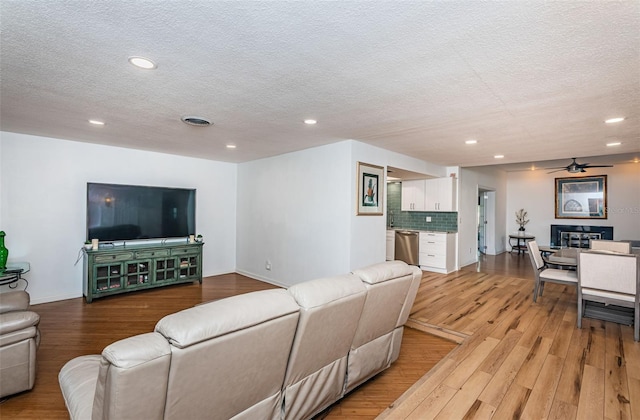 living room featuring ceiling fan, light hardwood / wood-style floors, and a textured ceiling